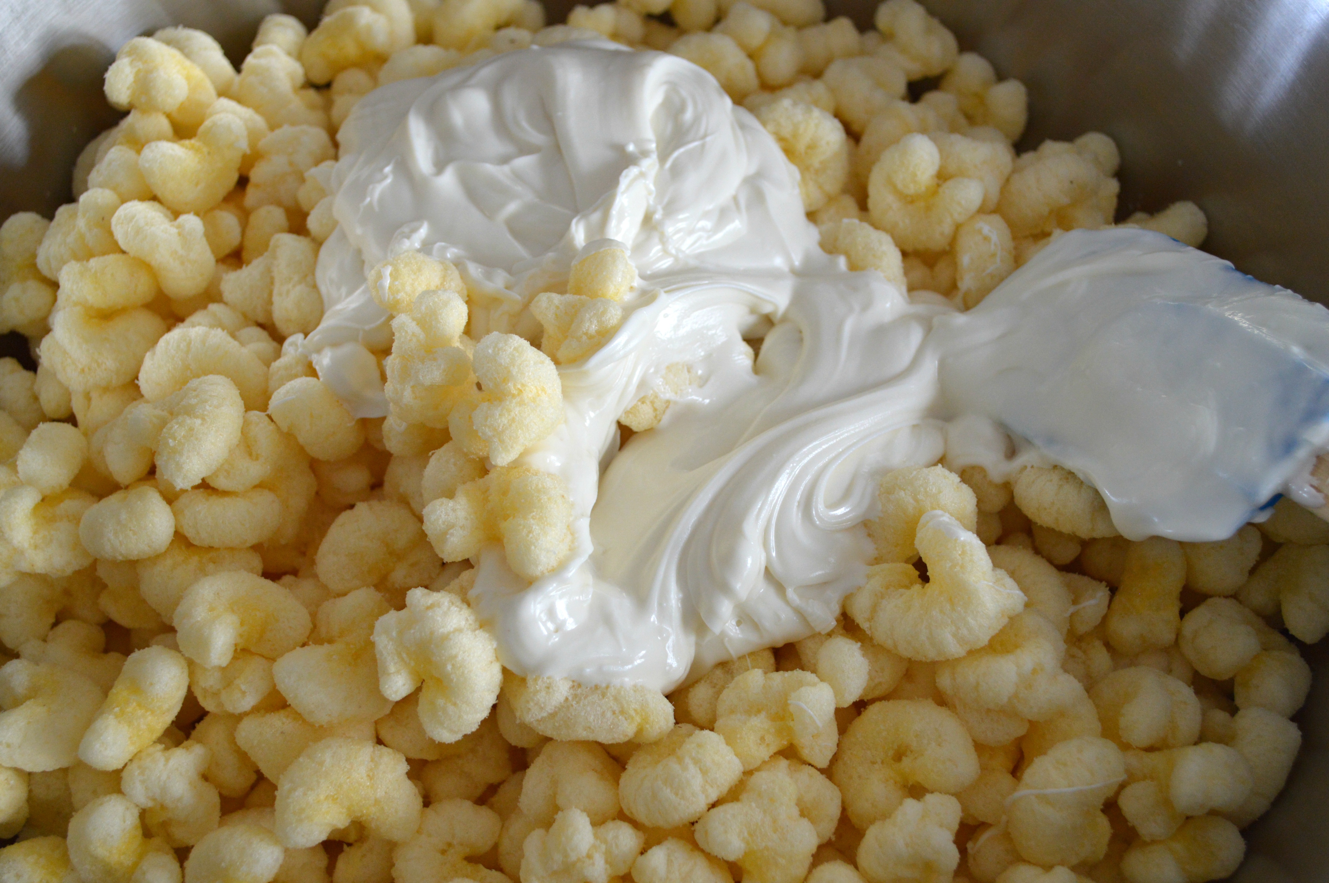 Corn Puffs, Puff Corn or Corn Pops in a large bowl with the melted white chocolate chips poured on top