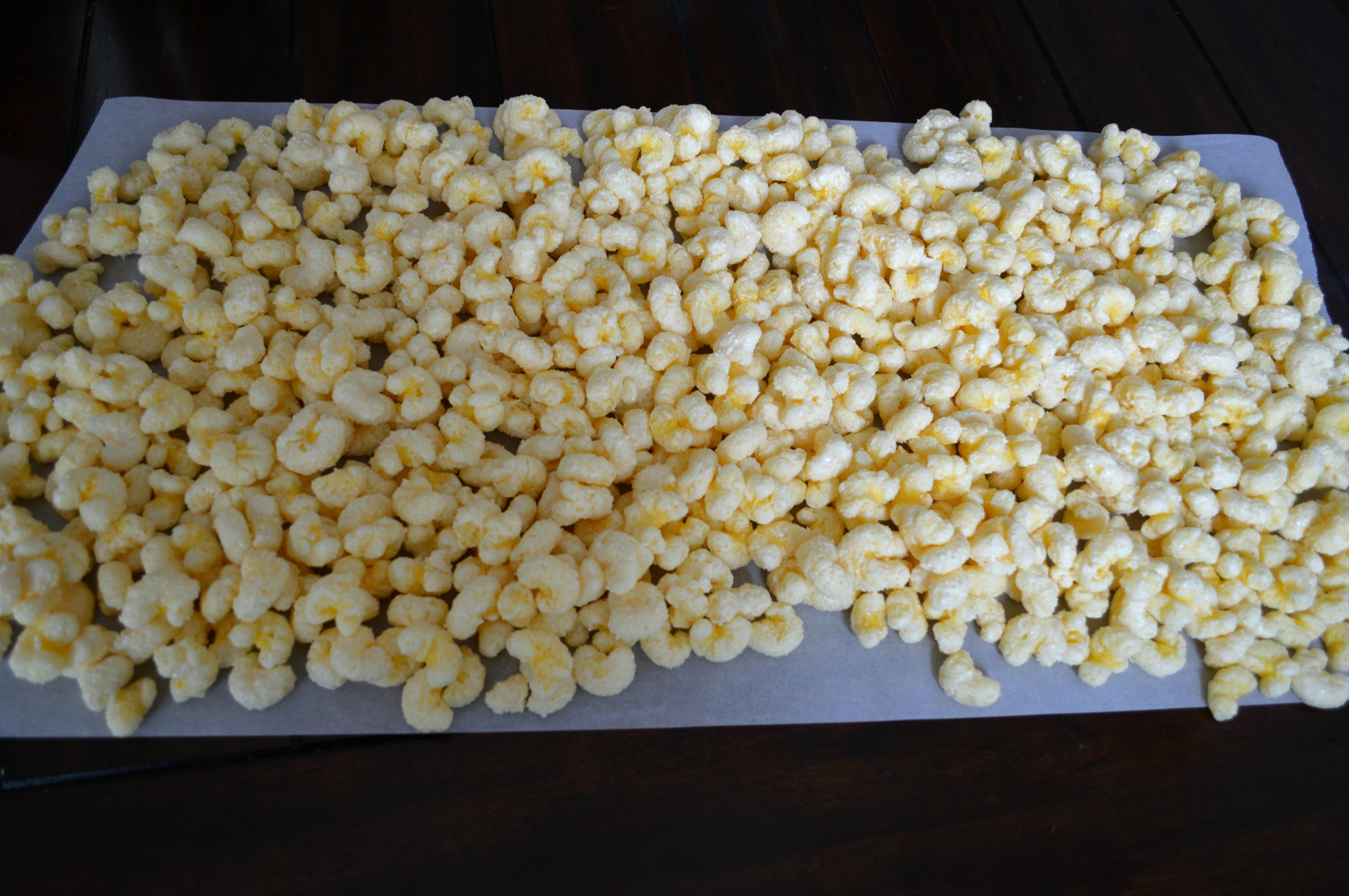 The Corn Puffs, Puff Corn or Corn Pops with the white chocolate chips stirred in completely and spread on a large piece of parchment paper or waxed paper to set up